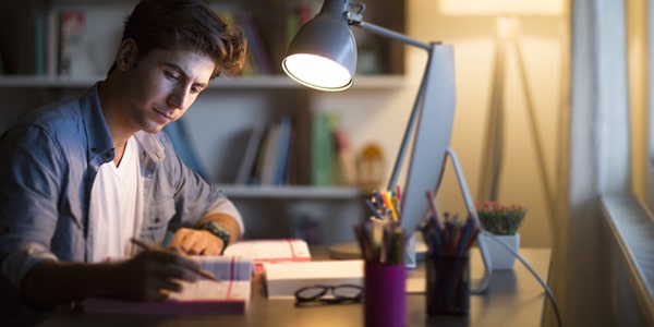 Hombre joven estudiante universitario leyendo textos con una computadora al frente
